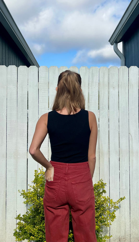 Person wearing a black top and red pants standing in front of a white picket fence with a blue sky.