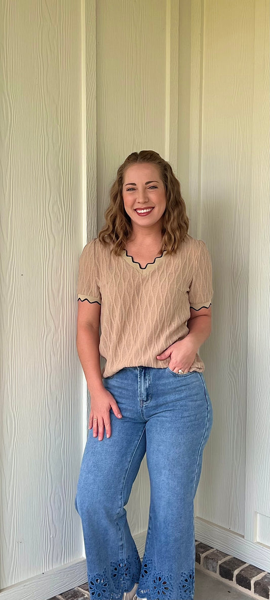 Woman wearing a beige top and blue jeans standing against a light-colored wall.