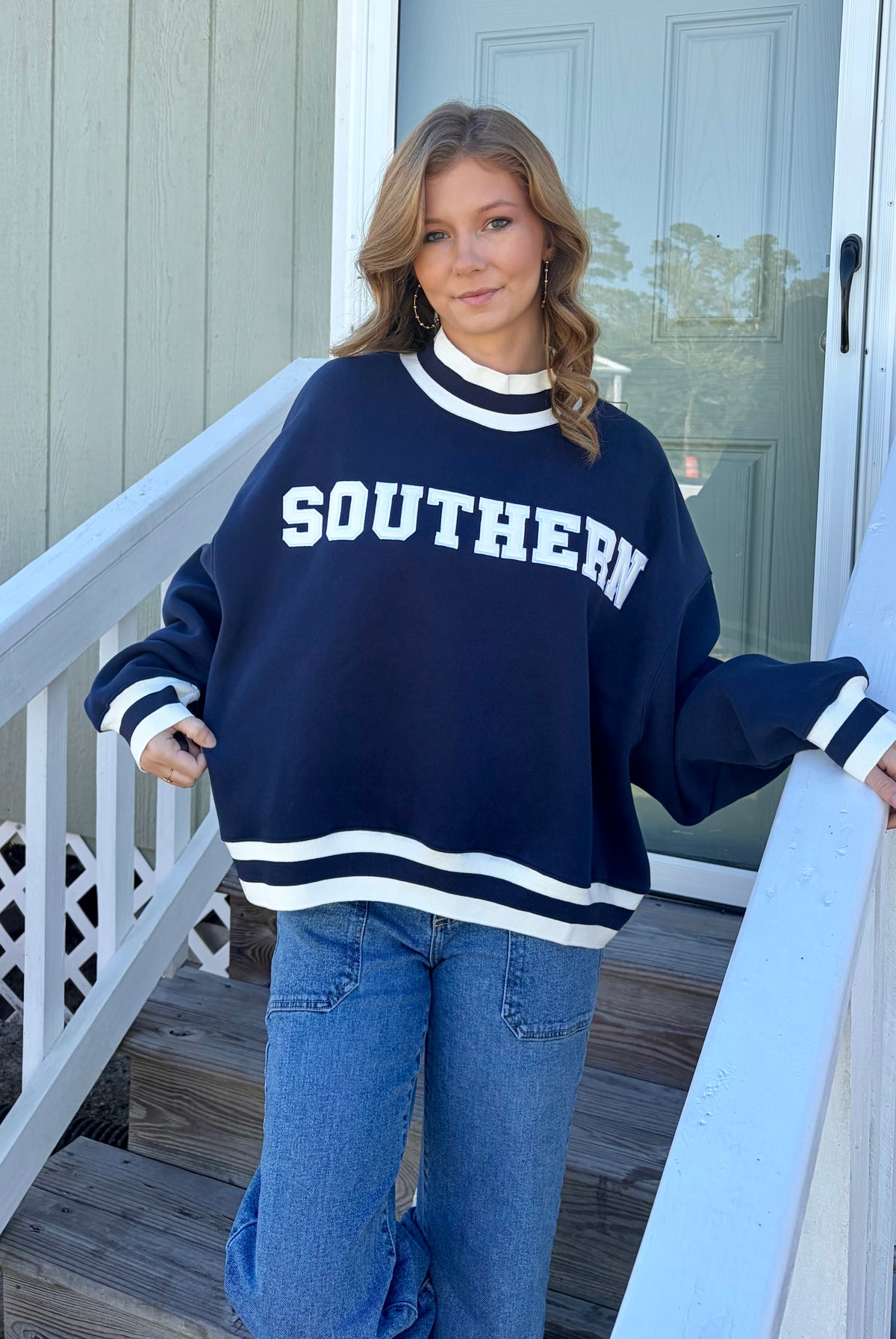A woman wearing a navy blue and white varsity-style sweatshirt with 'SOUTHERN' printed across the chest, paired with blue jeans, standing on outdoor wooden steps.