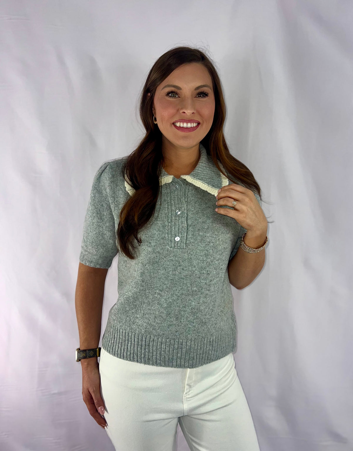 Woman wearing a green knitted polo shirt and white pants against a white background