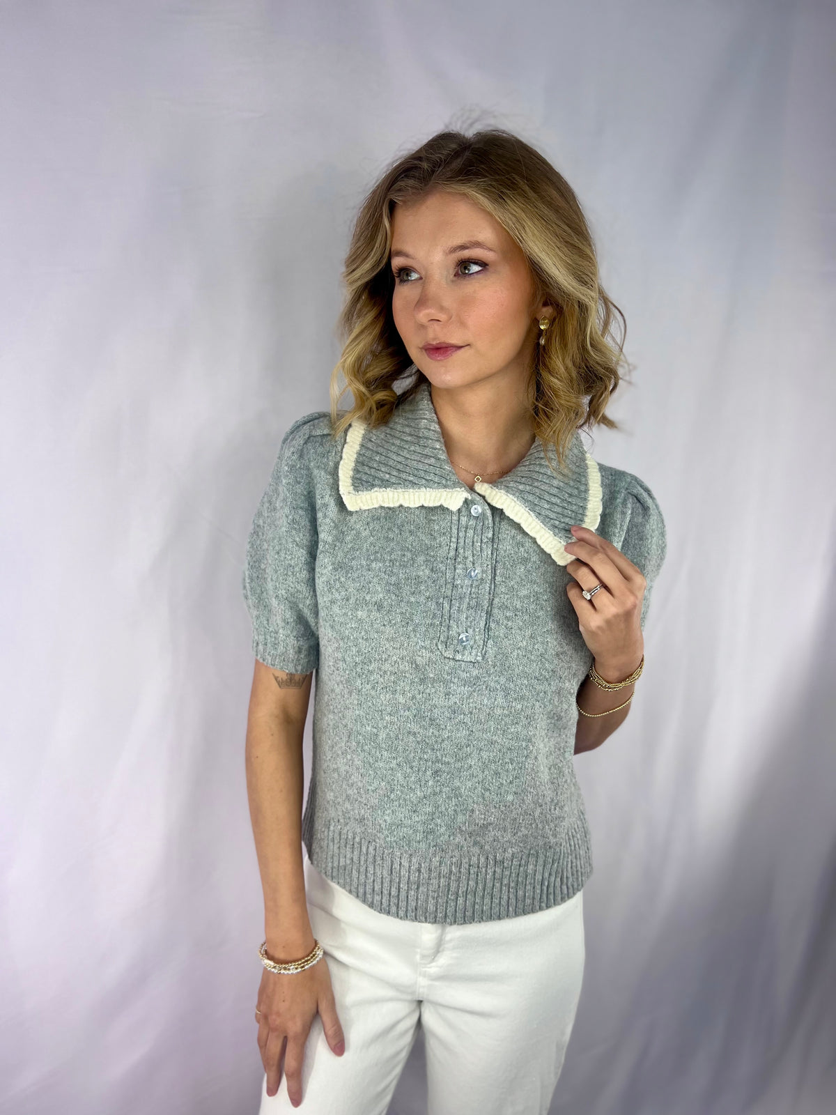 Woman wearing a gray sweater with a white collar against a plain background